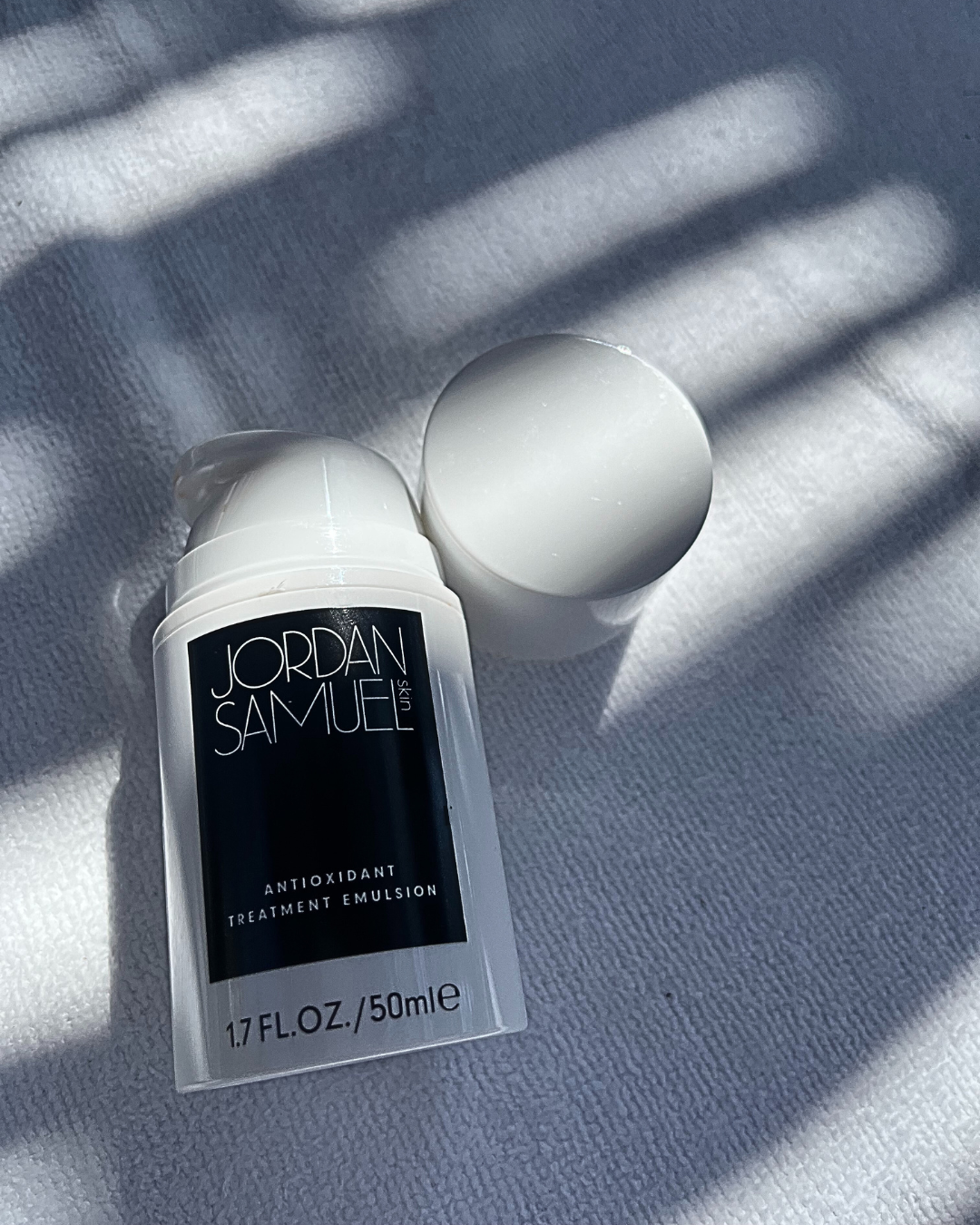 Antioxidant Treatment Emulsion lays on a white towel as sun streams through a pergola, casting it in shadows.
