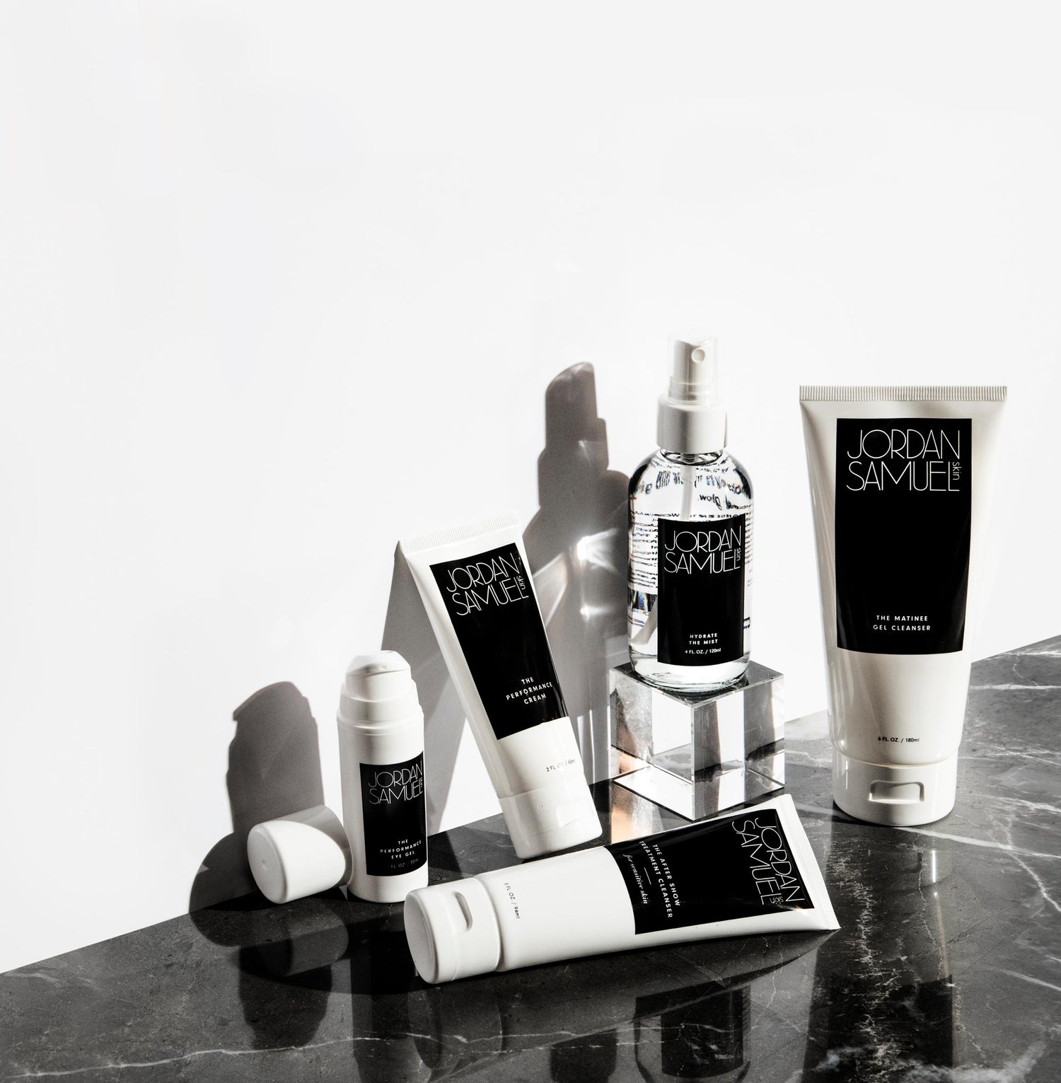 4 brightly-lit JSS products are arranged on a black marble surface up against a stark white wall