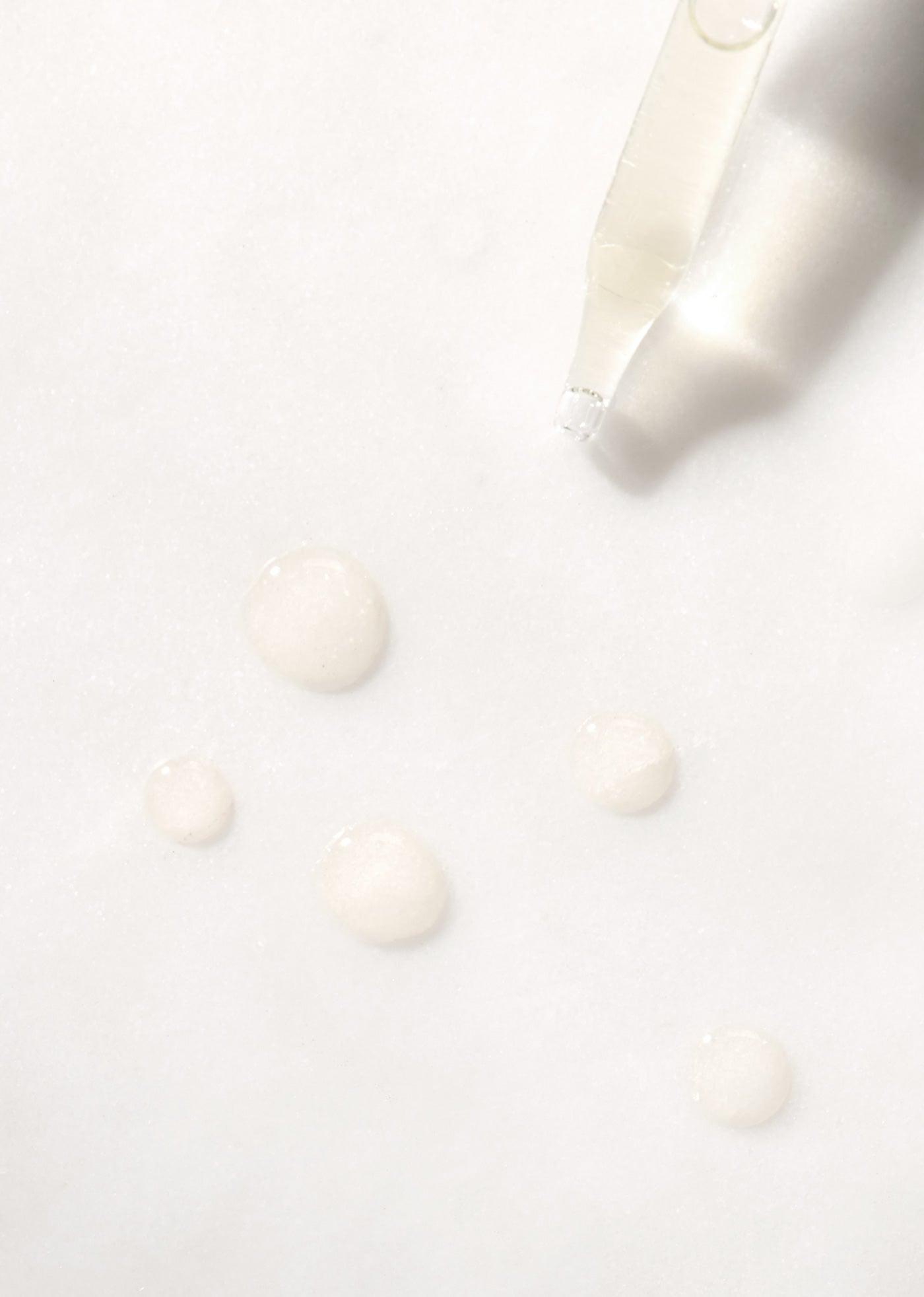 Tip of dropper with drops of translucent Retinol Treatment Oil on white background.
